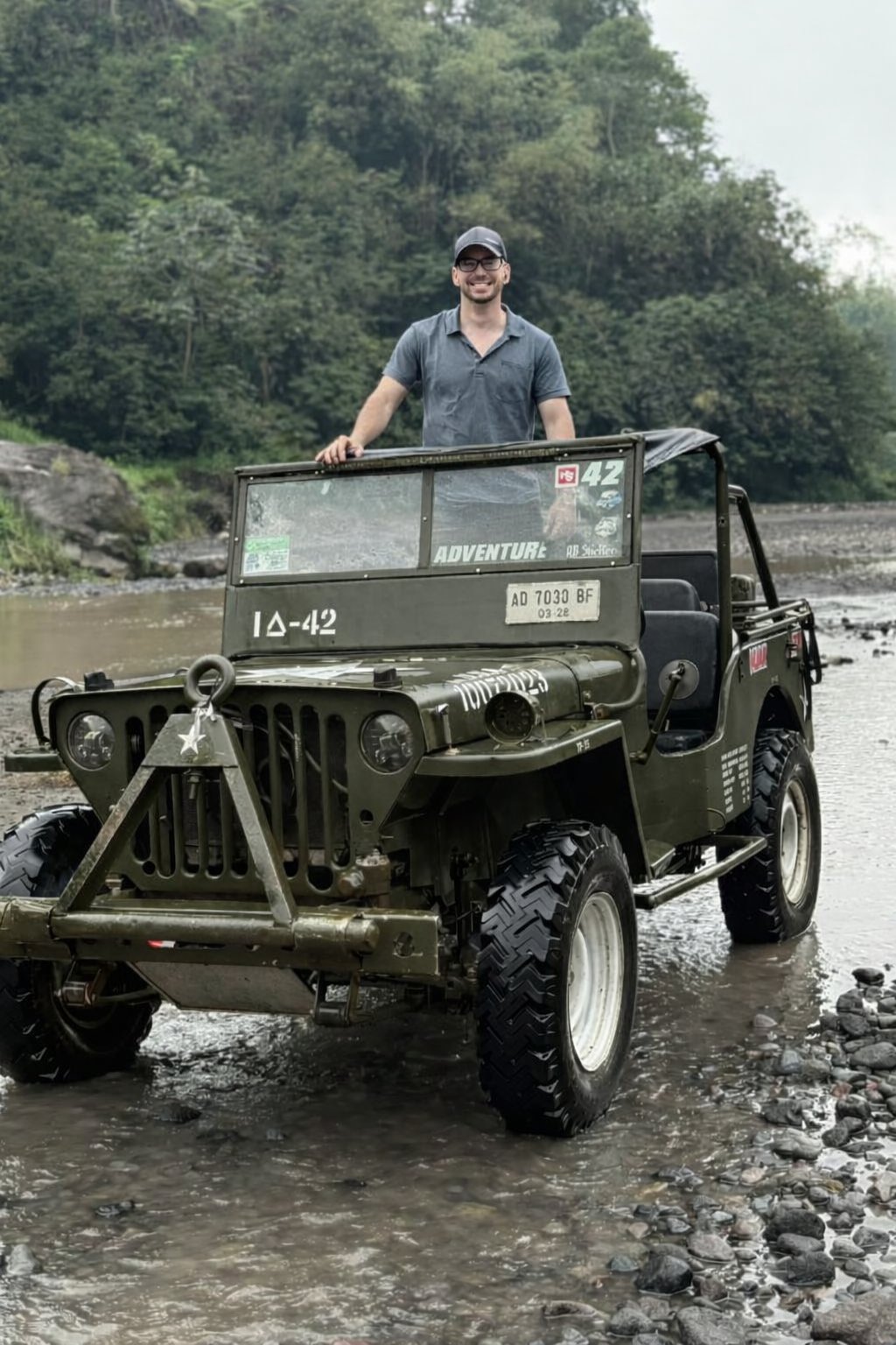 Koby, standing in a vintage jeep at a river